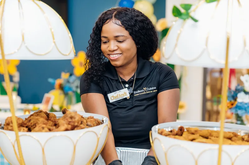 Smiling Chef Andi, wearing an Owner and Founder badge, serving at a buffet