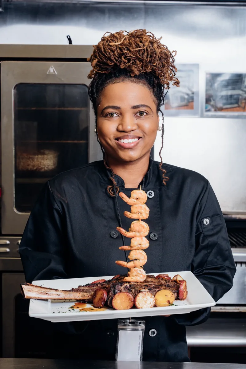 Chef in a kitchen presenting a plate of steak and shrimp