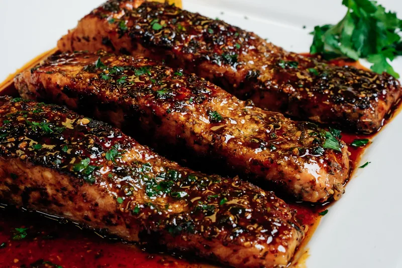 Glazed salmon fillets on a white platter with parsley