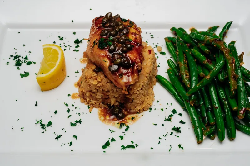 Plated fish over rice with green beans and a lemon wedge