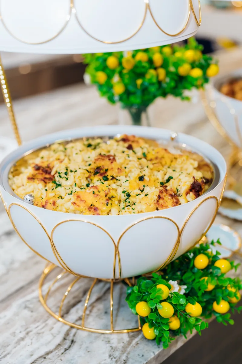Baked side dish in a white and gold buffet vessel with lemon styling