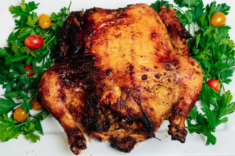 Whole roast chicken on a platter garnished with parsley and tomatoes